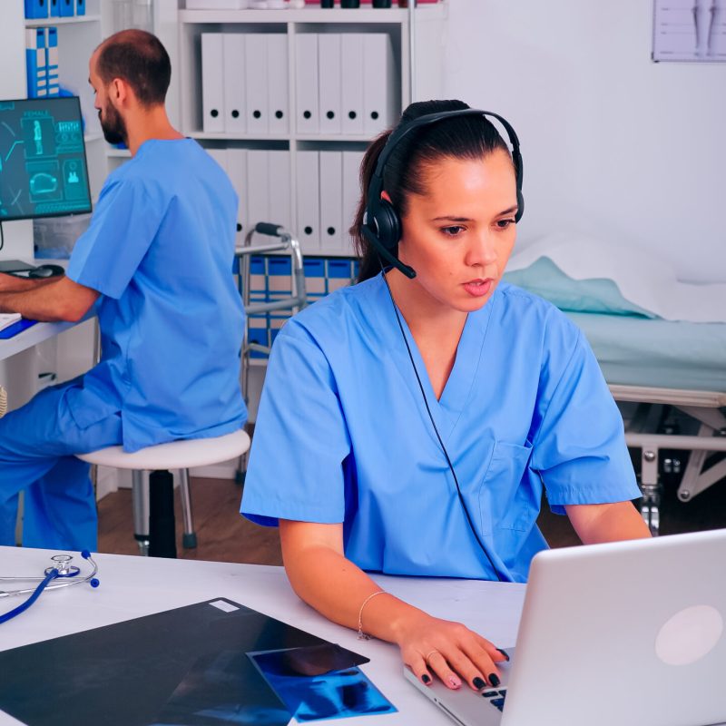 Surgeon assistant using headphones in hospital answering to patients calls for appointments and consultations. Healthcare physician in medicine uniform, doctor nurse helping with telehealth communication